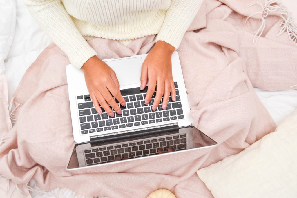A cropped image of a woman sitting on a bed, using her laptop - how to write an about me page for a blog.
