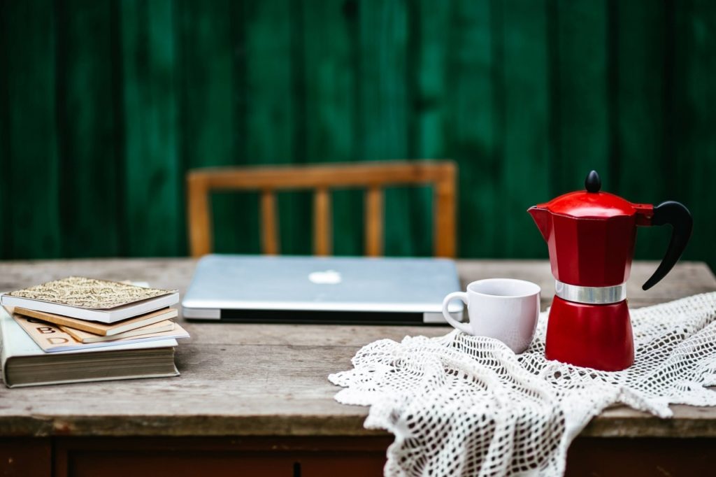 Table with a red coffee pot and a white cup and a closed laptop - the best blogging tools for new bloggers. 