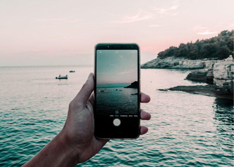 Holding a phone to take a photo of a shoreline at sunset - Nature Hashtags for Instagram
