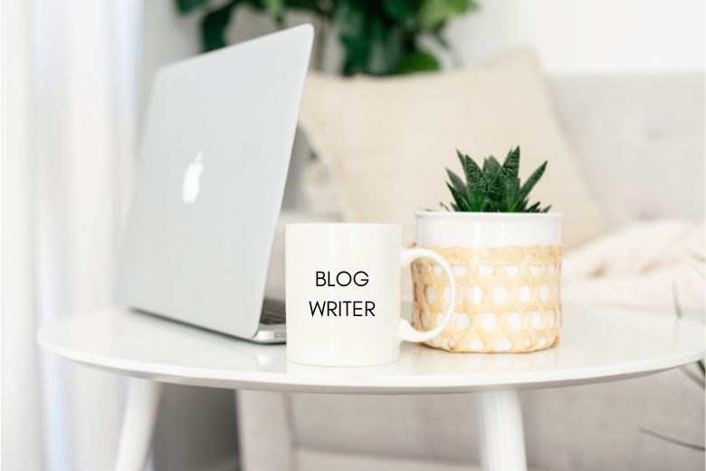 Laptop, mug and potted plant on a small table - answering the question of how many posts should you have before you launch your new blog. 