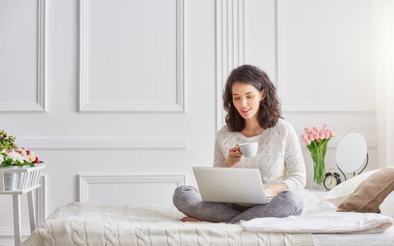 Woman drinking a cup of coffee in bed while using a laptop - Stressful Blogging Mistakes New Bloggers Make