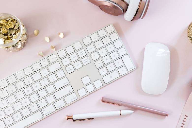 A pink desktop with a laptop keyboard, mouse and pen - best Facebook groups for bloggers.