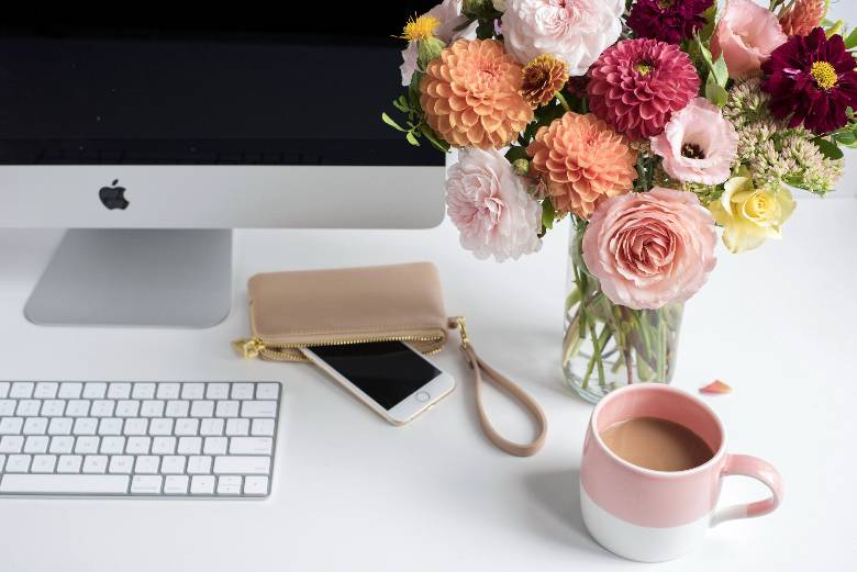 Desktop with computer and cup of coffee and vase of flowers - how to keep your blog organized.