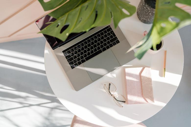 Laptop on a white table with a pink notebook - how to promote affiliate links.