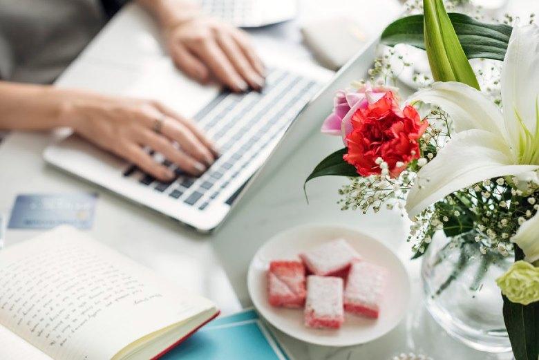 Woman typing at a laptop keyboard with flowers in the foreground - top WordPress plugins for blogs.