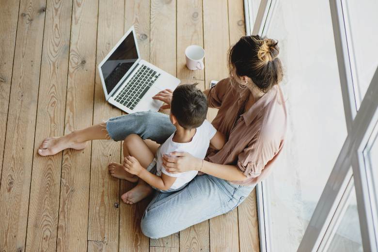 Mom with a child in her lap, using a laptop - top down view - mom blog post ideas.