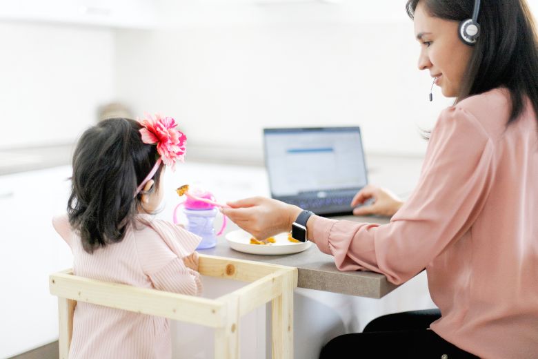 Mom working at a computer while feeding child - 300+ mom blog post ideas