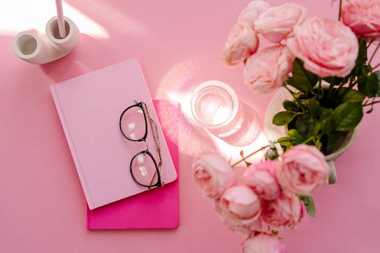 Pink desktop, pink flowers in a vase, pink notebook and glasses - May blog post ideas. 