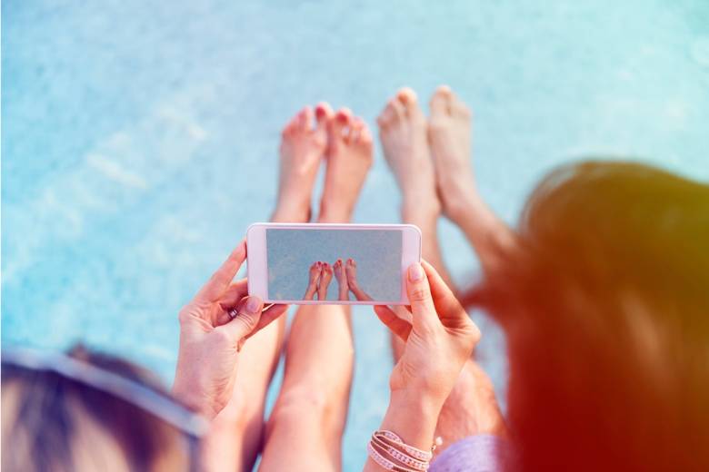 Summer Hashtags For Instagram - two women looking their phone showing an image of their feet in the pool.