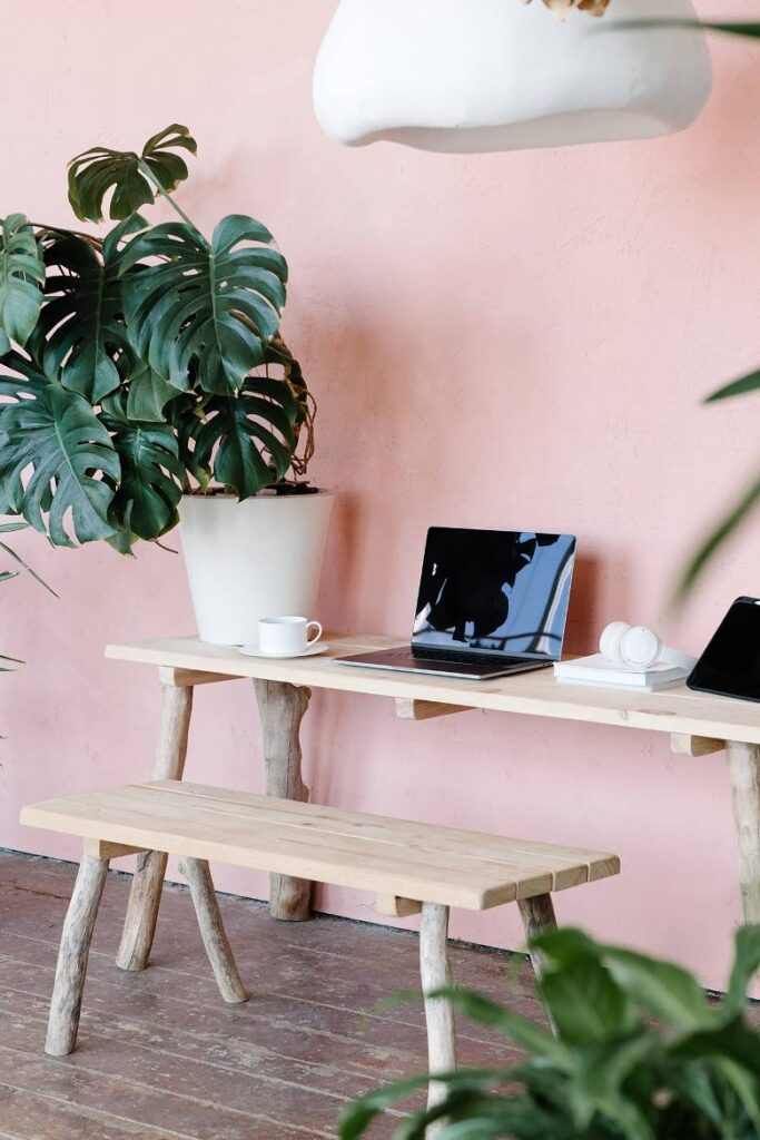 Laptop on a table by a pink wall. 