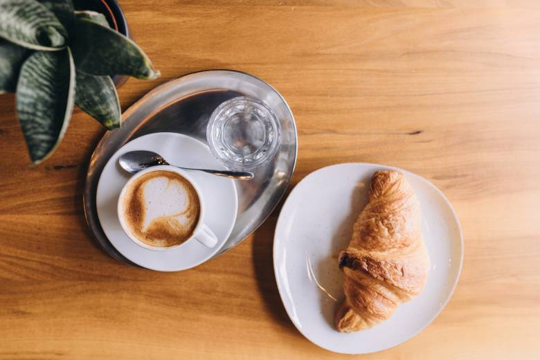 Croissant and coffee on a table - top down view - productivity tips for starting an online business.