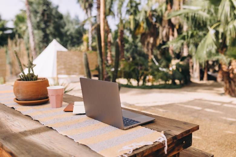 A laptop on a wood desk  in a beach setting - how to make money with a travel blog. 