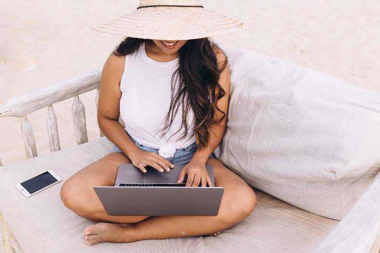 Woman typing on a laptop while one a beach - how to start a travel blog.
