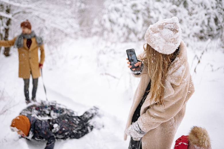 Couple playing in the snow with the woman taking a photo with her phone - Winter quotes for Instagram posts and captions,