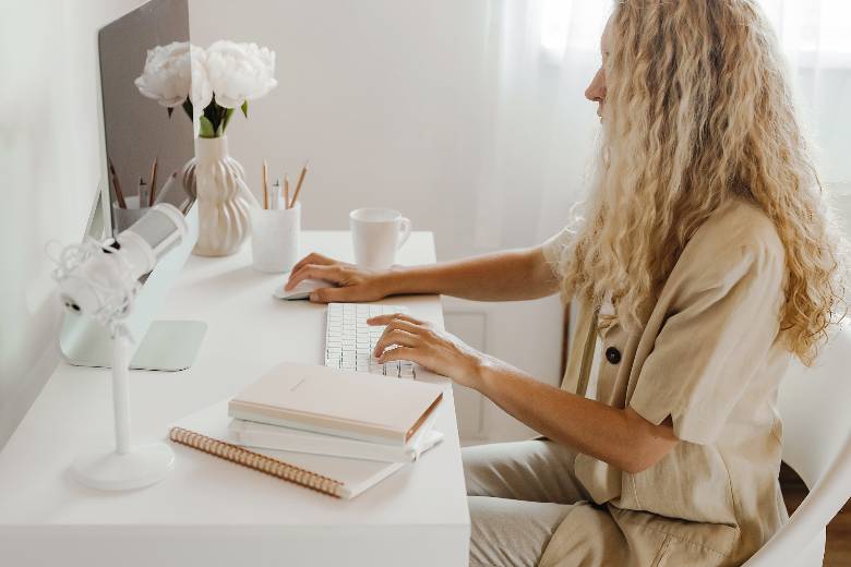 Woman with blonde hair sitting at a desk working on her computer - how to become a confident blogger. 
