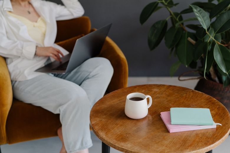 Faceless woman using a laptop with a table and notebook in front of her - how to become a confident blogger.