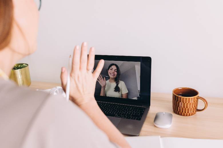 Woman waving to another woman during a video call on a laptop - how to connect with other bloggers.