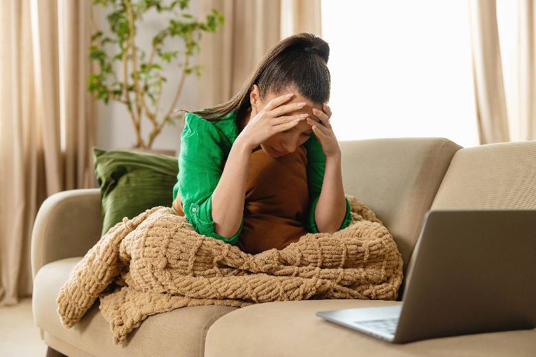 Woman holding her head in her hands, while sitting on a sofa with a laptop - how to backup your WordPress website.