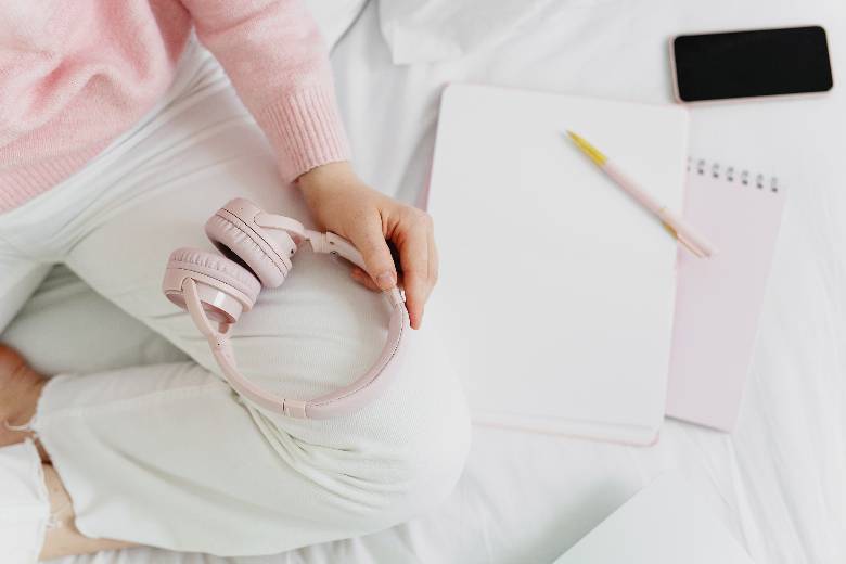 Lifestyle blog niches - woman's hands with a notebook and headphones on a white bed.