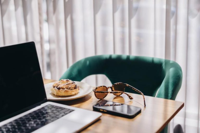 A table with a laptop, and green chair, phone and sunglasses - tips for beginner bloggers from blog coach, Margaret Bourne.