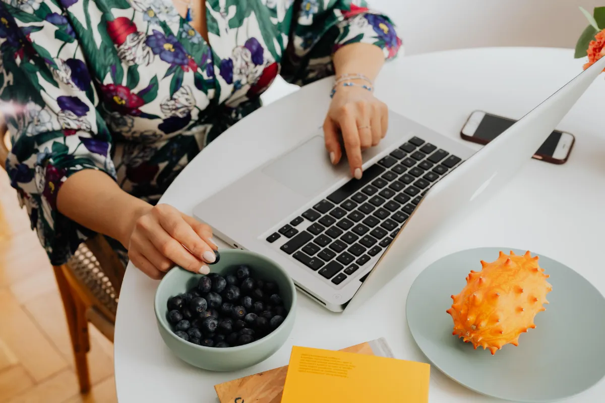 How to Back Up Your WordPress Blog Step-by-Step 1 Faceless woman using a laptop with a bowl of blueberries as a snack - how to backup a WordPress blog.