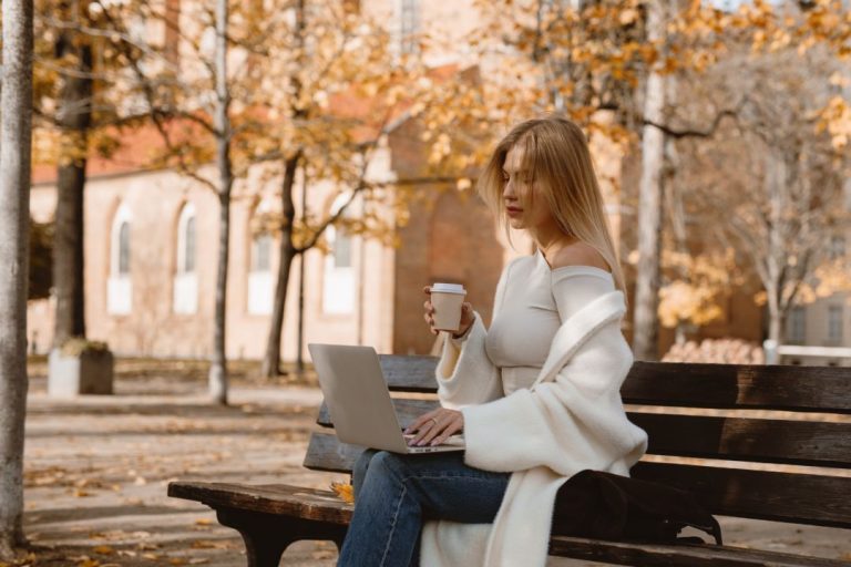Over 120 Fresh Fall Blog Post Ideas For Lifestyle Blogs (2026) 10 Woman sitting outside in the Fall with a laptop and coffee cup - Fall blog post ideas.
