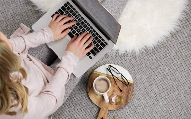 100+ Winter Blog Post Ideas: Festive & Seasonal Topics 1 Faceless woman typing on a keyboard with cozy blanket and warm winter clothes - winter blog post ideas for lifestyle bloggers.