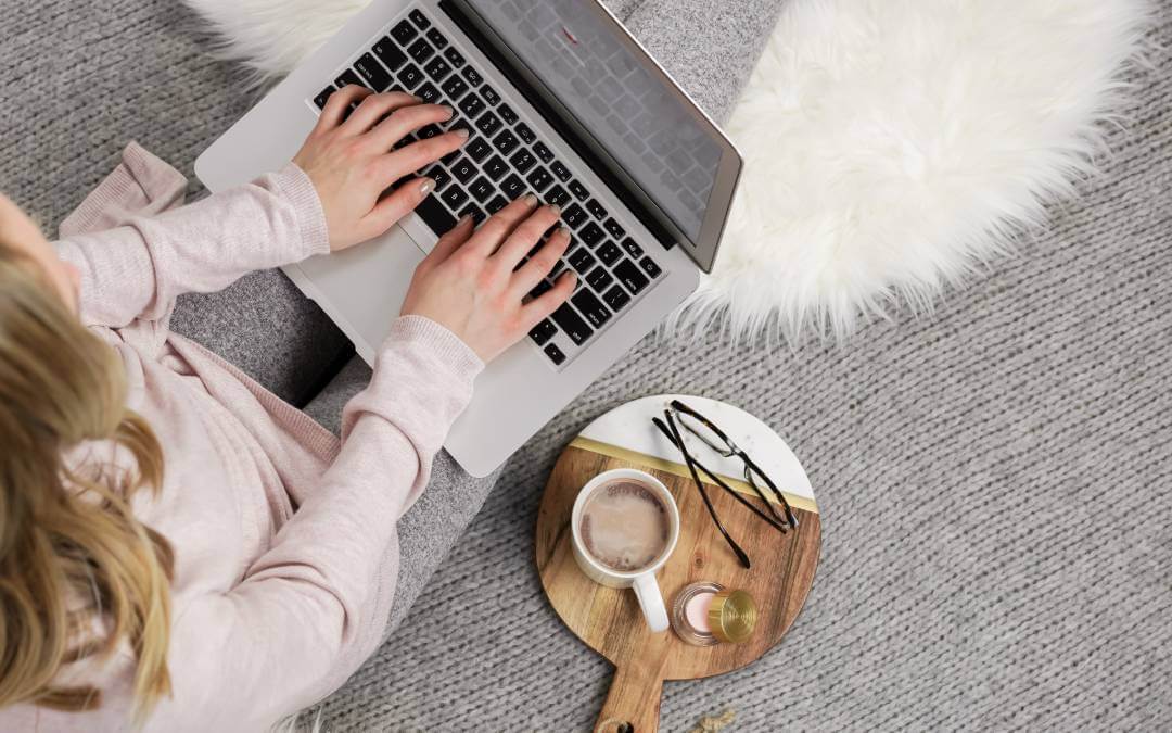 100+ Winter Blog Post Ideas: Festive & Seasonal Topics 1 Faceless woman typing on a keyboard with cozy blanket and warm winter clothes - winter blog post ideas for lifestyle bloggers.